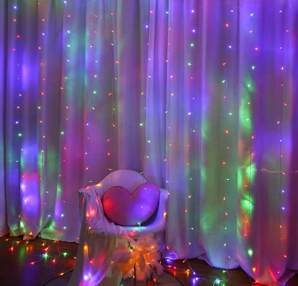 Cortina luces LED multicolor en habitación con sillón y cojín corazón